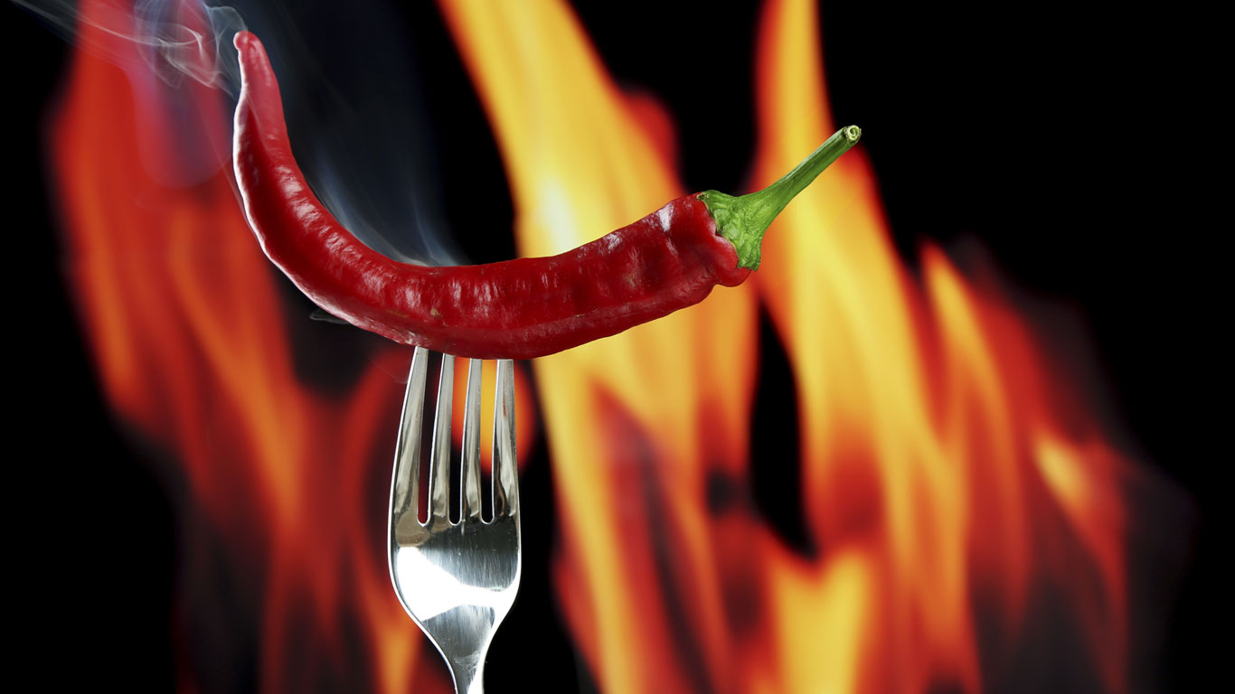 Rote Peperoni auf einer Gabel mit Flammen im Hintergrund